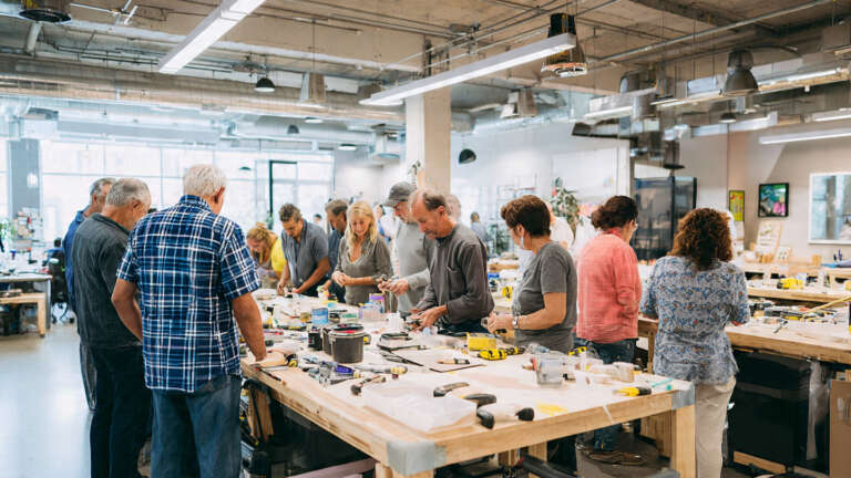 Homeowners attending a hands-on DIY home improvement workshop, learning practical skills from an instructor in a well-equipped workshop space