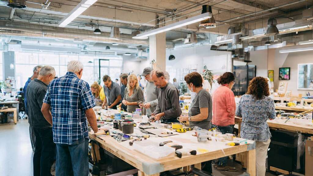 Homeowners attending a hands-on DIY home improvement workshop, learning practical skills from an instructor in a well-equipped workshop space