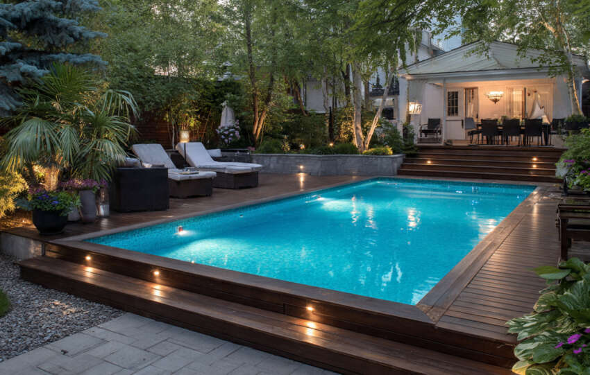 Modern above ground pool with wooden deck and outdoor seating in a sunny backyard.