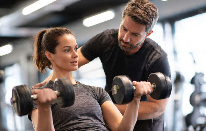 Personal trainer assisting a client with resistance training in a gym.